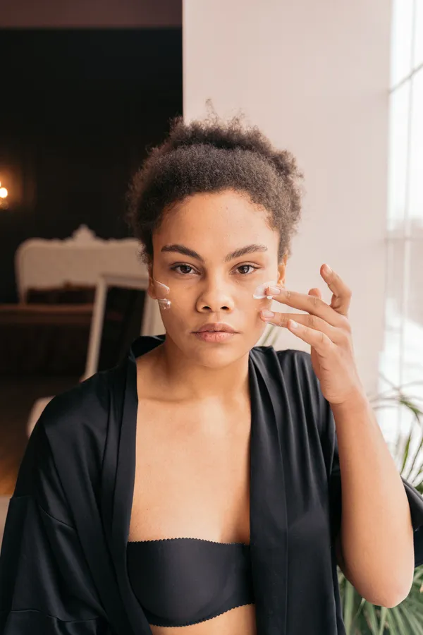 Woman applying cream beneath her eyes in soft window light